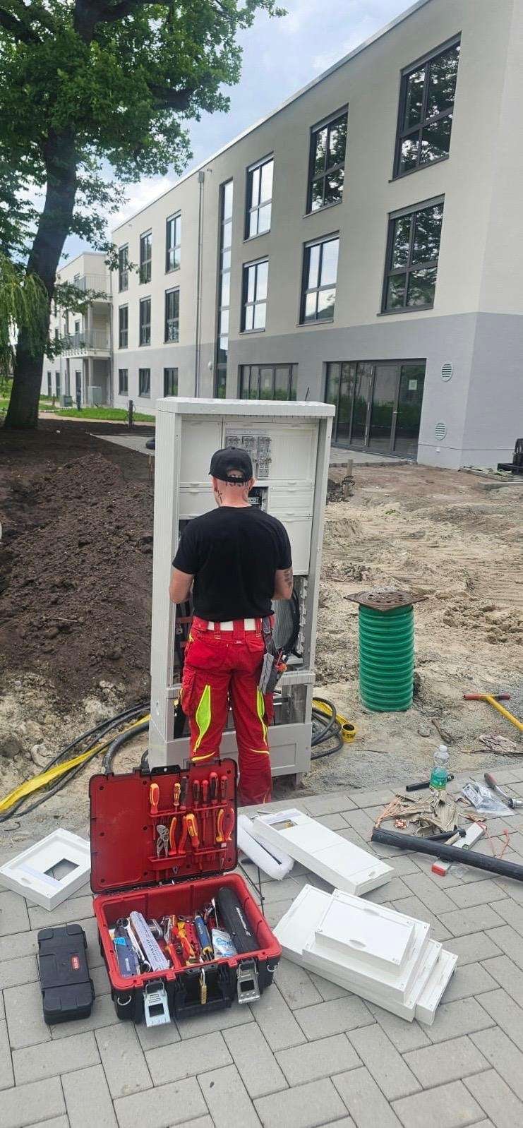 Technik pri montáži prípojkového piliera, vedľa neho otvorený kufor s náradím