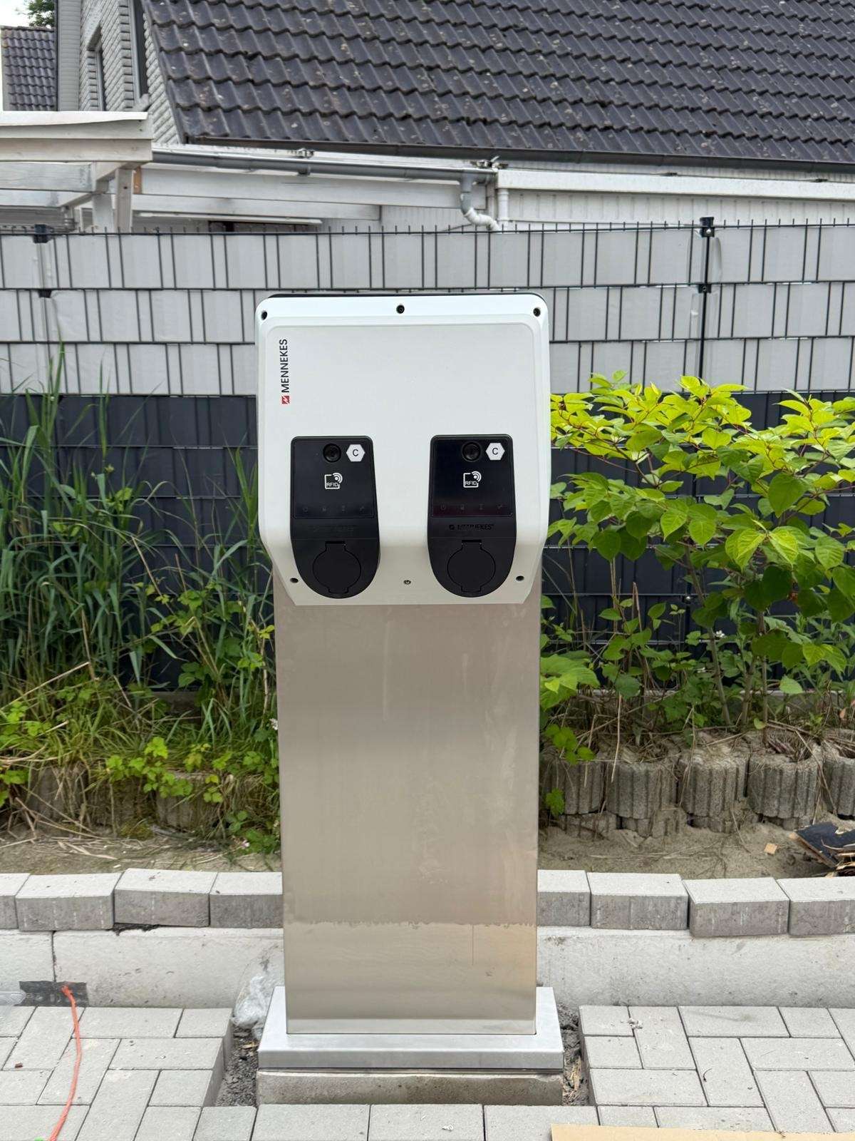 Dvojitá nabíjacia stanica pre elektromobily na nerezovom podstavci pri chodníku