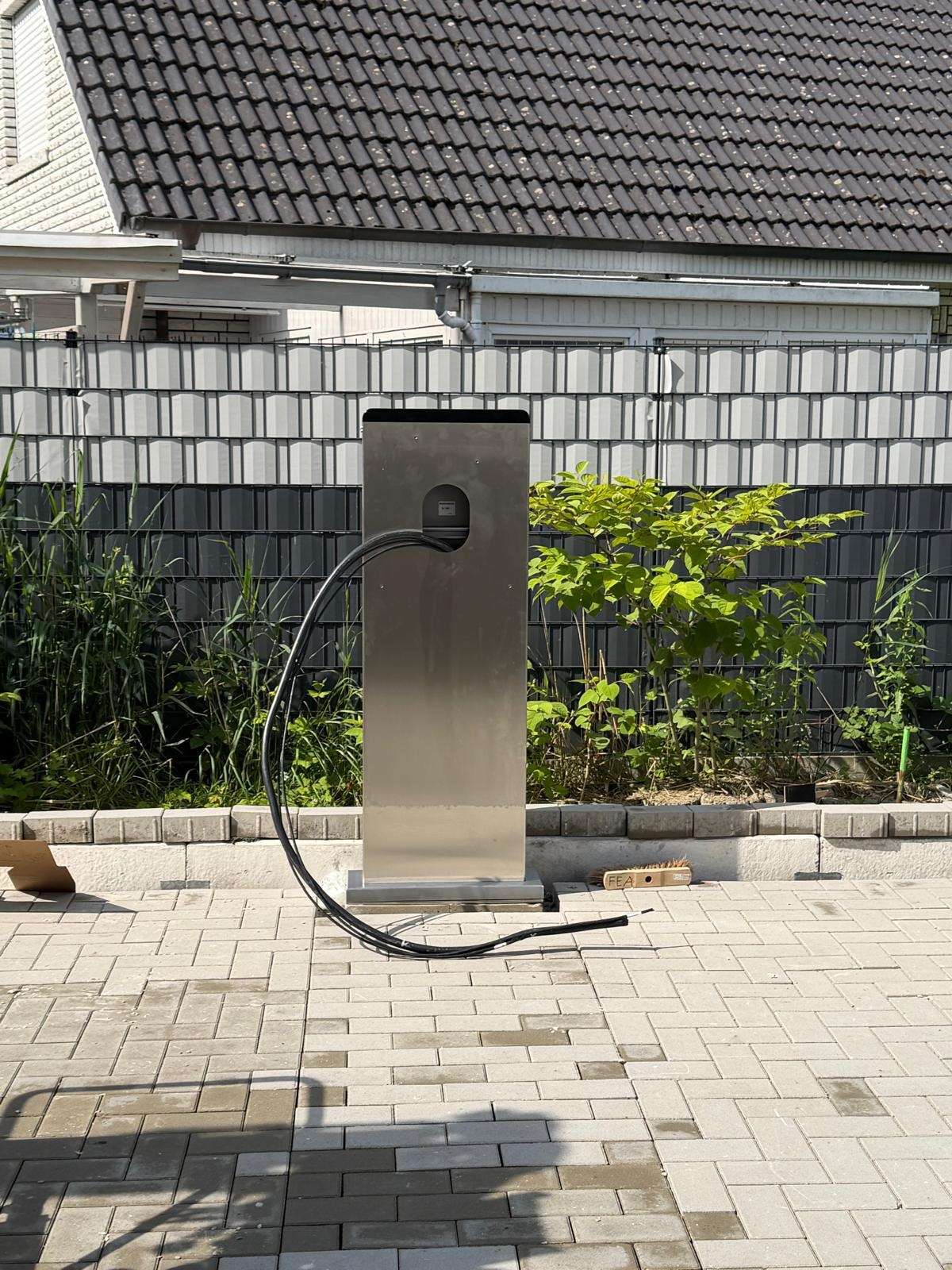 Nabíjacia stanica pre elektromobil na podstavci pri rodinnom dome, kábel zavesený na držiaku